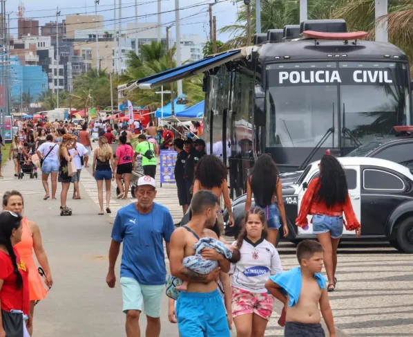 Avenida movimentada com muitas pessoas durante um evento, com policiamento visível e atividades ao ar livre, destacando a presença da Polícia Civil. Delegacia Móvel da PCPR é ponto de referência nos eventos do Verão Maior Paraná